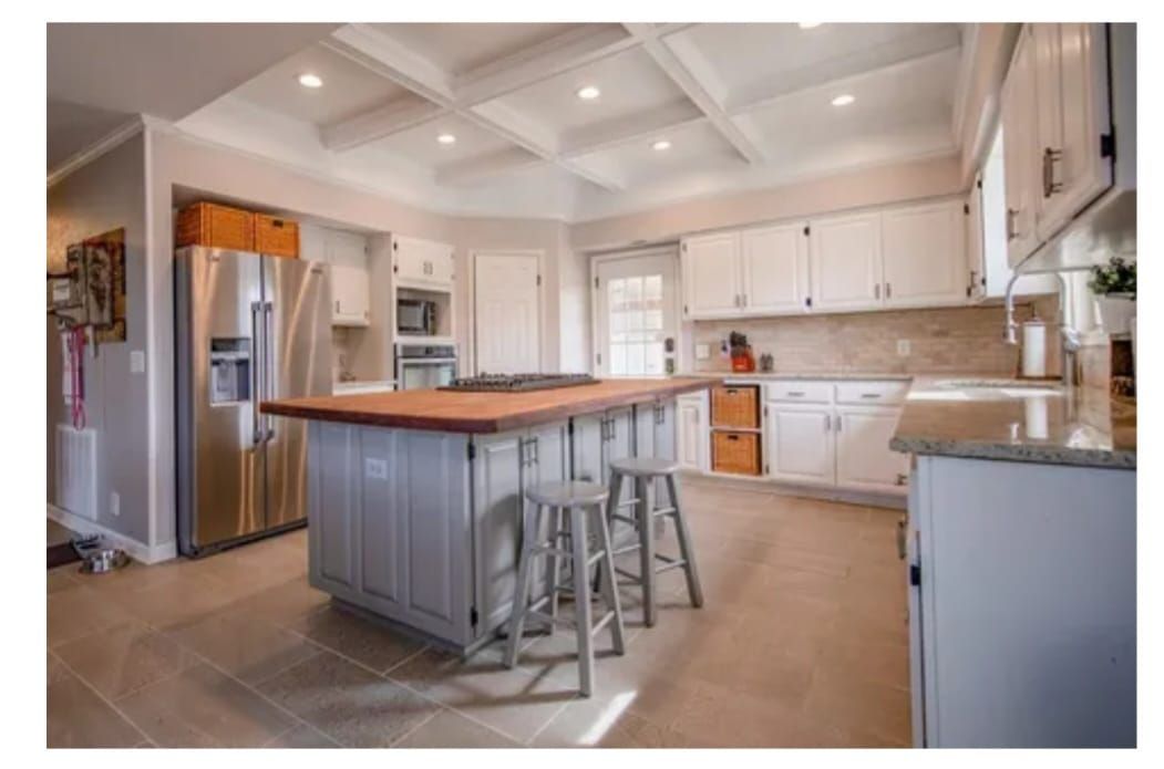 Kitchen with white cabinets, wooden island, stainless steel appliances, and tiled floor.