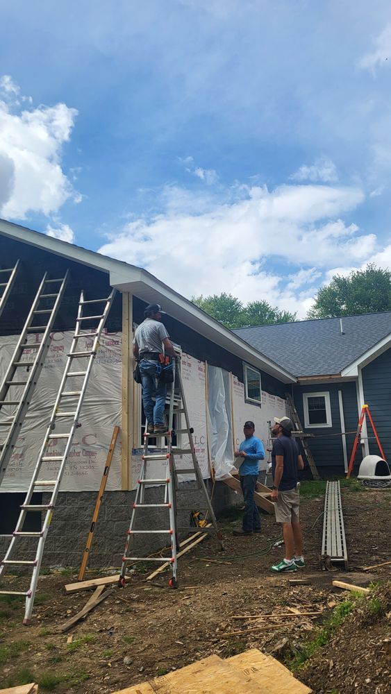 Construction workers installing siding on a house under a blue sky.
