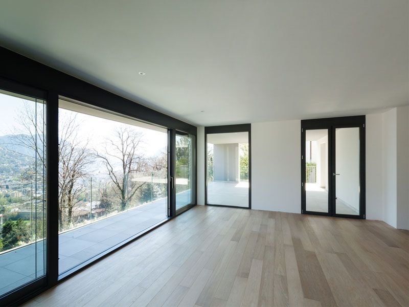 Empty, modern room with large windows overlooking a scenic landscape, wood floor, and white walls.