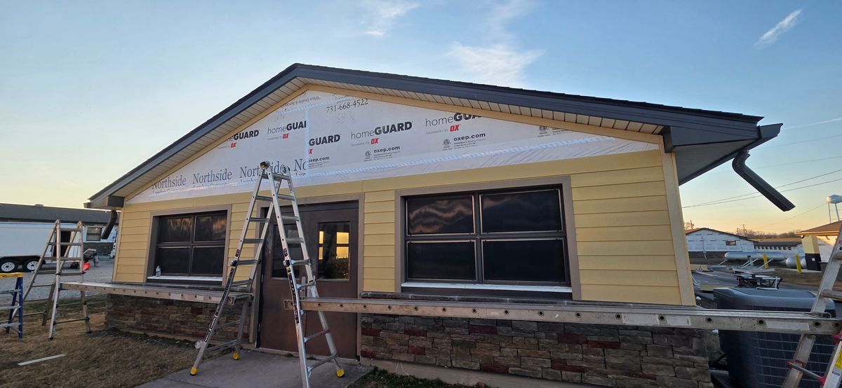 Exterior of a house under construction; yellow siding, black roof, and windows with covering.