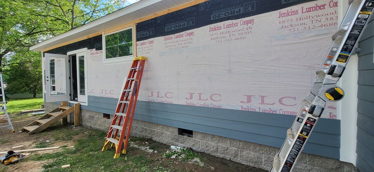 Construction site: house with siding, ladders, and building materials.