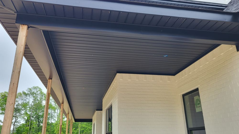 Black soffit and trim installed on a covered porch. White brick wall and wooden supports are visible.
