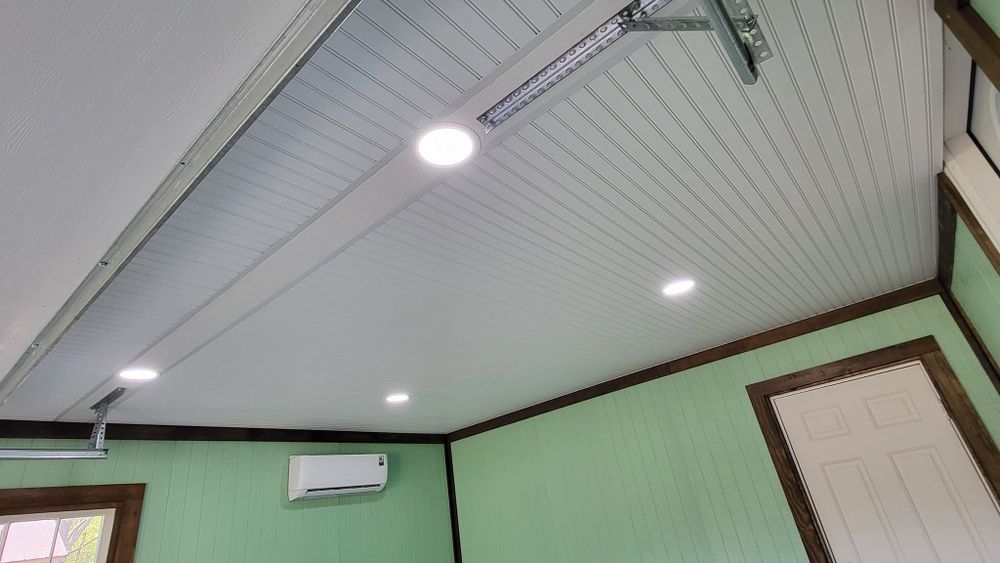 Green-walled room with a white panel ceiling, recessed lights, and air conditioner; brown trim around the door and windows.