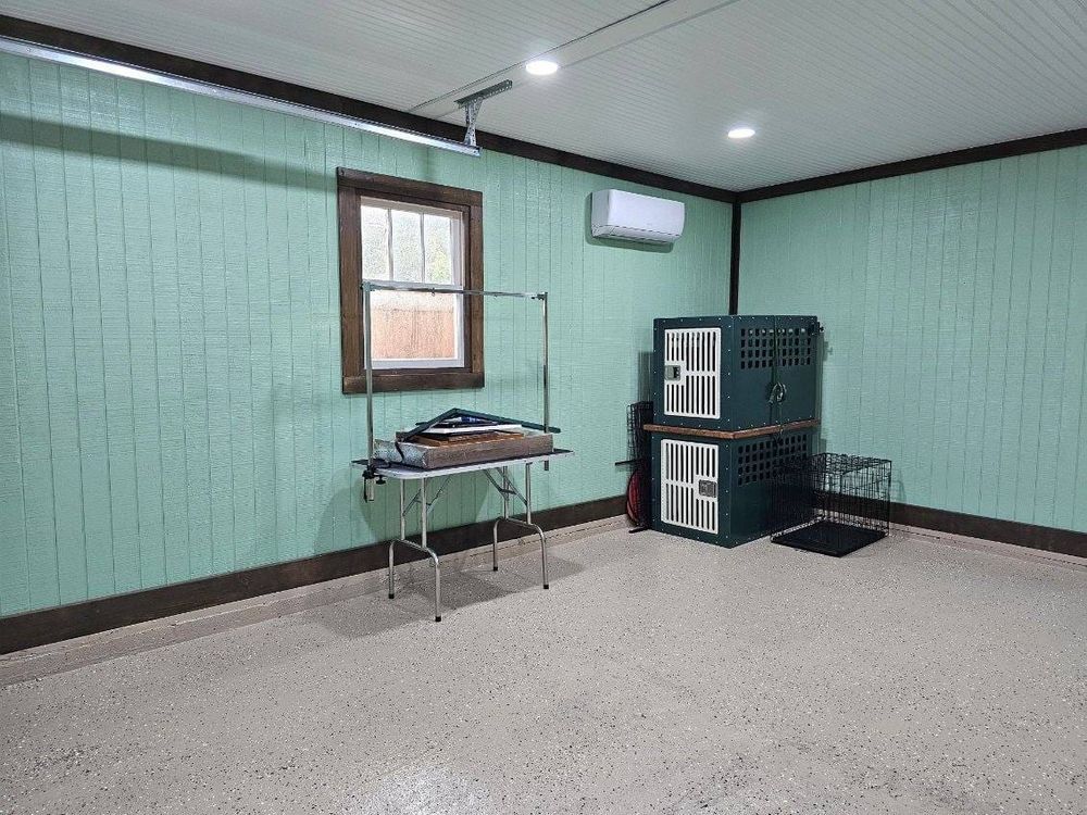 Interior of a dog grooming room with a grooming table, crates, and an air conditioner. Light green walls, gray floor.