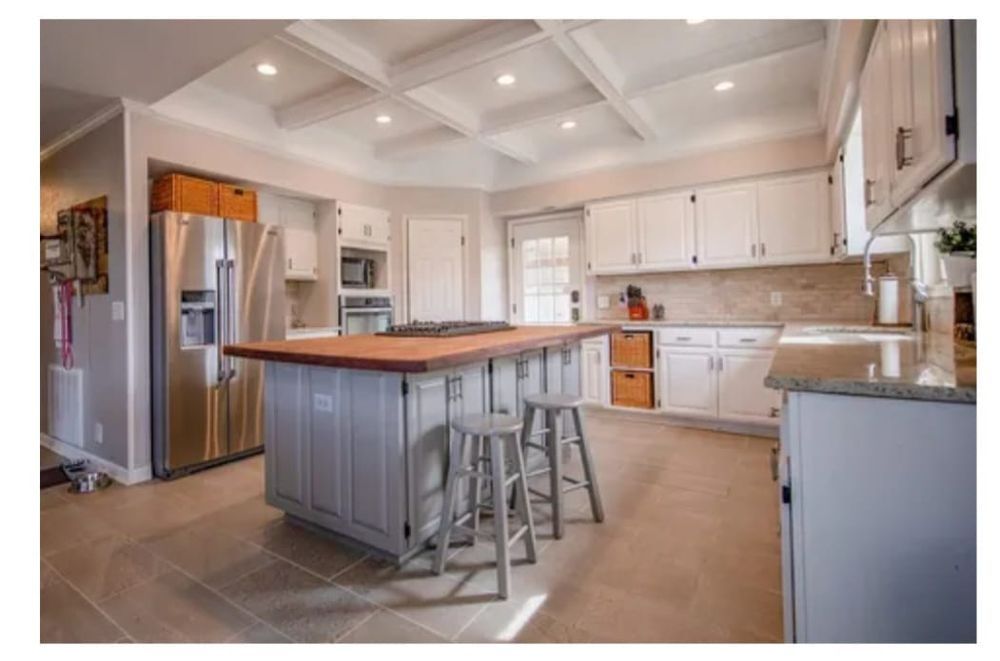 Spacious white kitchen with island, stainless steel refrigerator, and wood-topped island with stools.