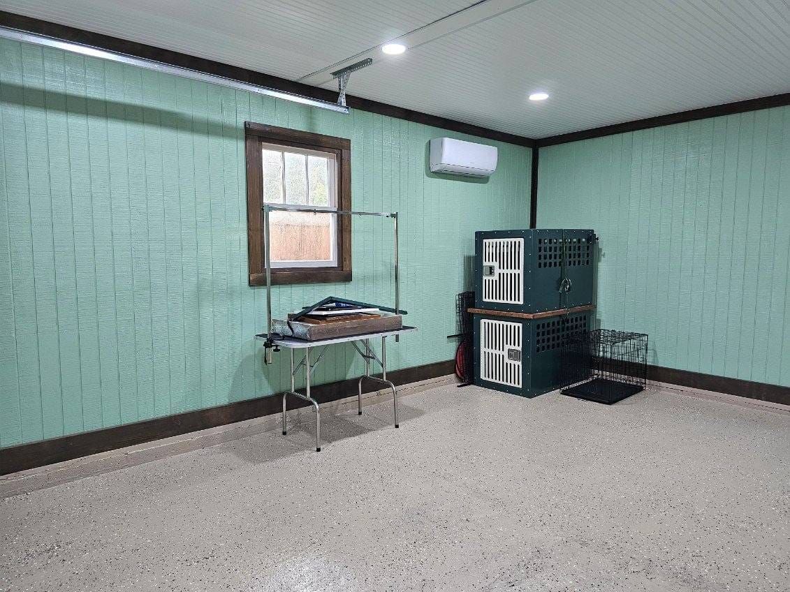 An empty dog grooming room. Green walls, a window, grooming table, crates, and air conditioner. Beige speckled floor.