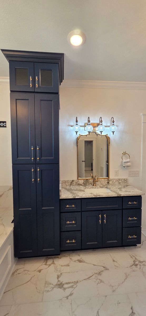 Bathroom with navy cabinets, marble countertop, and floor. Vanity mirror and lighting.