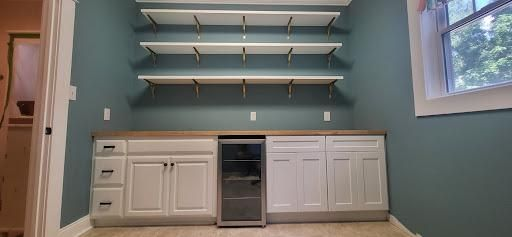 Built-in cabinetry with shelving, a wine fridge, and a window against a teal wall.