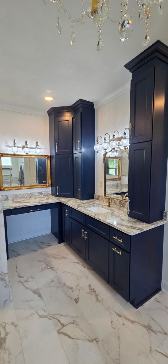 Bathroom with blue cabinets, marble countertop and flooring, gold accents, and a chandelier.