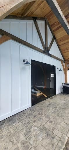 White building with dark entry, wooden beams, and a concrete patio.