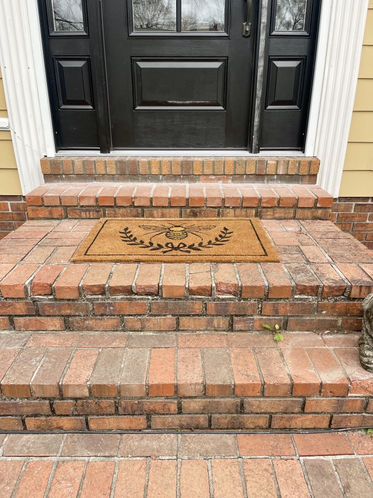 Brick steps leading to a black front door with a welcome mat displaying a bee design.