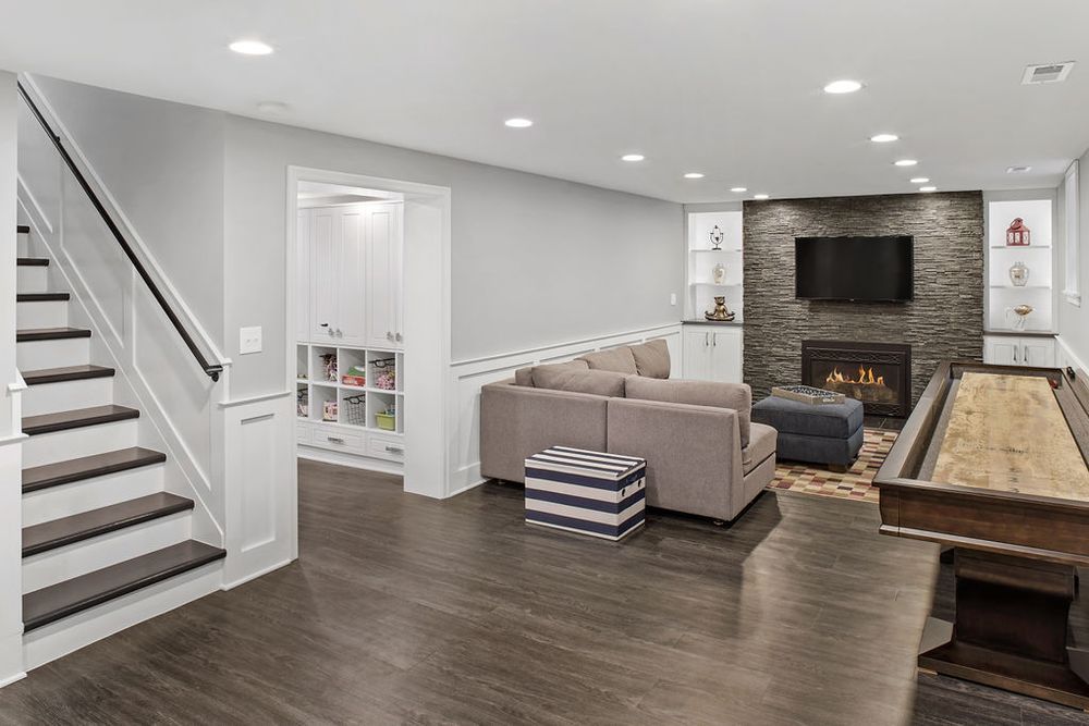 Basement living room with gray walls, sofa, fireplace, shuffleboard, and built-in storage.