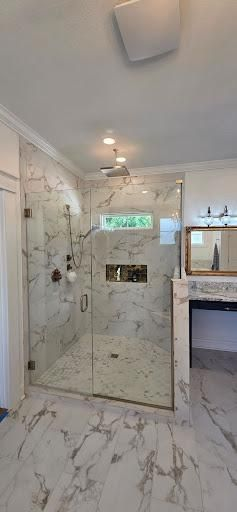 Luxurious marble-tiled shower with glass doors in a bathroom. Recessed shower niche and matching floor tiles.