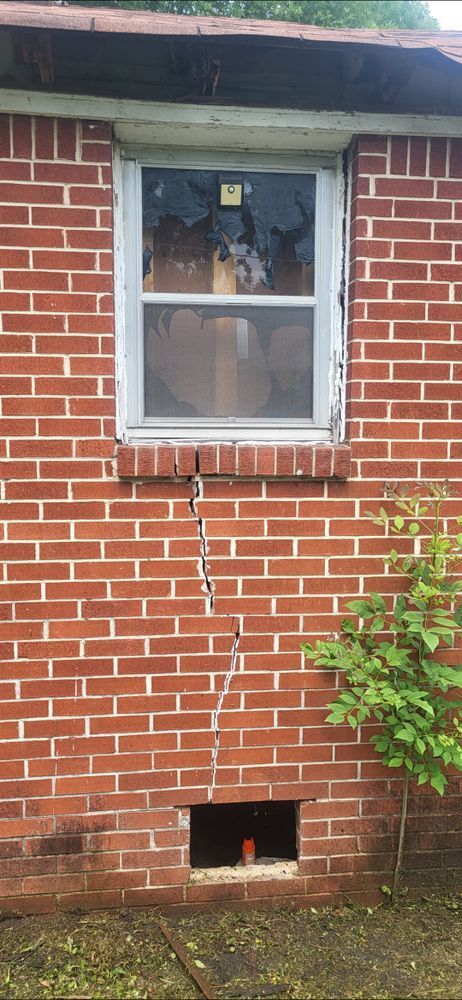 Brick building with a broken window and a large vertical crack in the wall. There's a small opening near the bottom.
