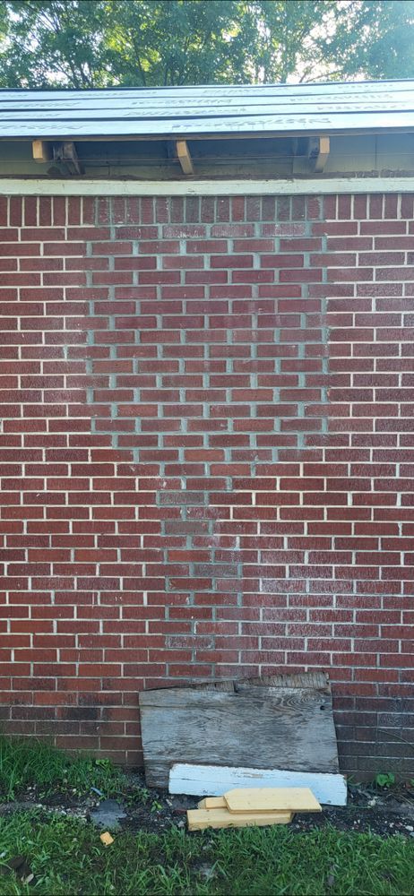 Red brick wall with weathered appearance. A section has darker discoloration. Wood and concrete debris rest at the base.
