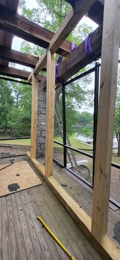Construction of a screened porch; wooden frame with a stone chimney. Trees and water in the background.