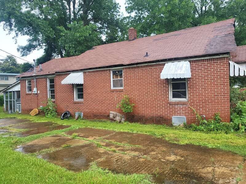 Red brick house with a weathered roof, three small windows, and metal awnings.