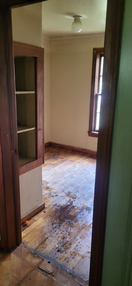 Interior view of a room with a damaged wooden floor, empty shelves, and a window.