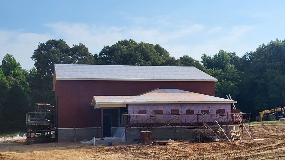 Red building with a flat roof under construction; surrounded by trees and clear sky.
