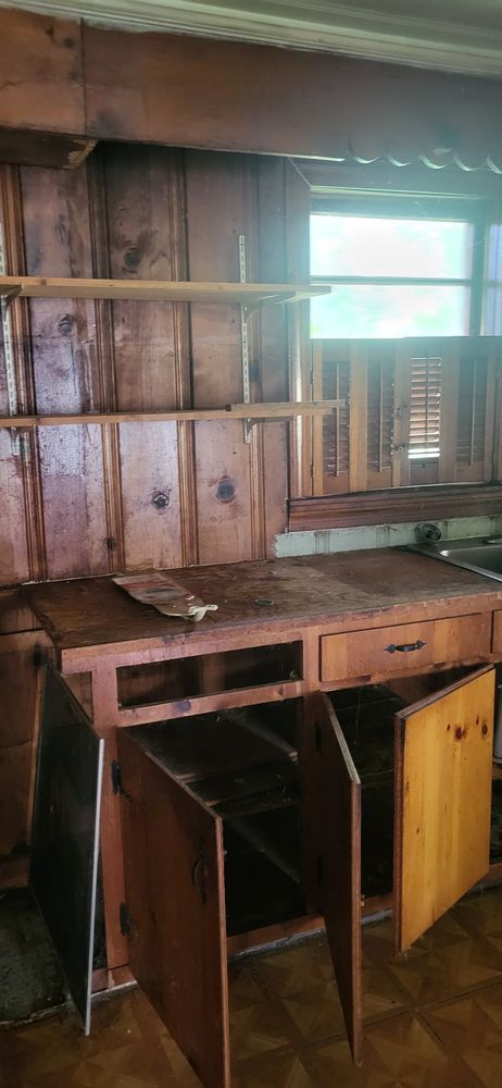 Wooden cabinetry in a room with a window. Cabinet doors are open, shelves are above, and the wood is aged.