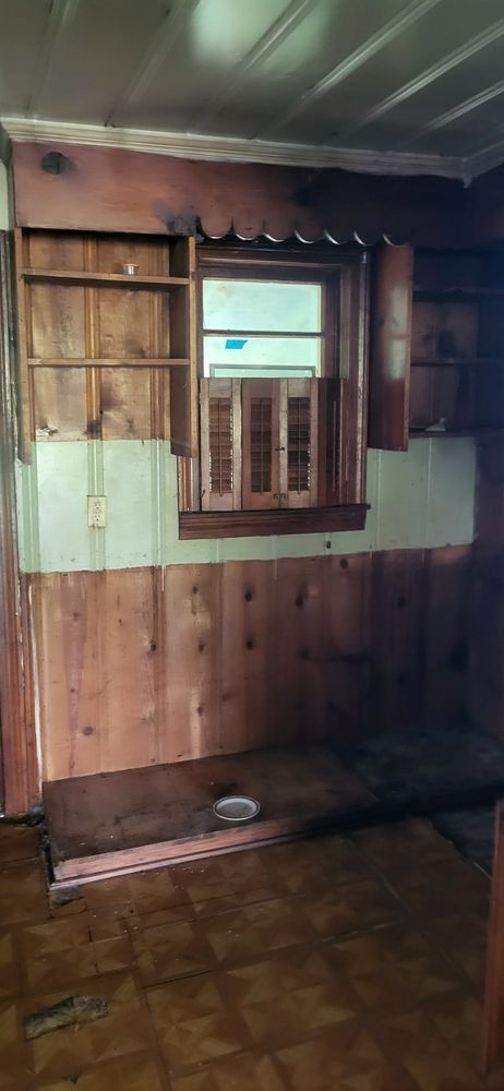 Interior room with wood paneling, shelves, and a window with an air conditioner.