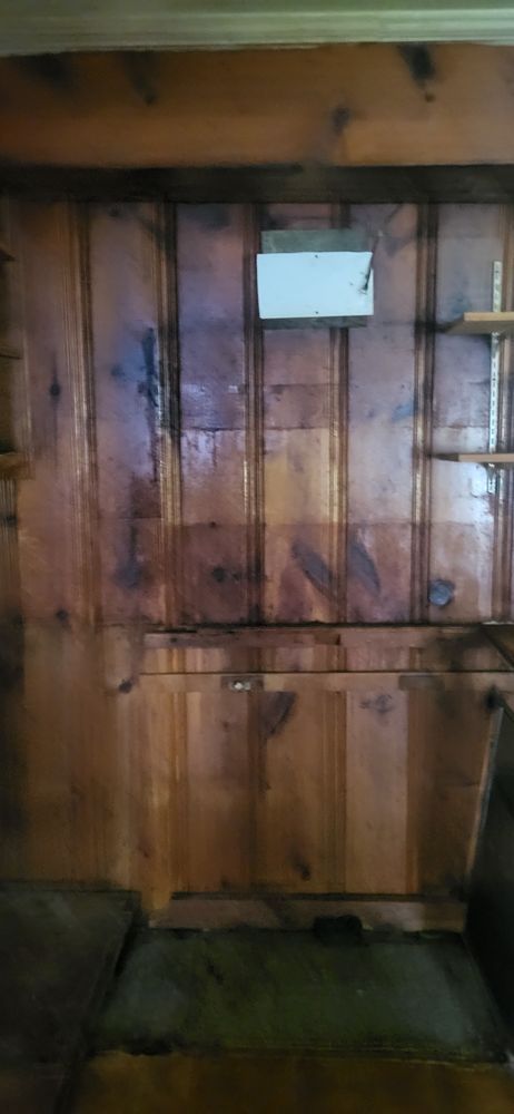 Wooden paneled wall with a small white rectangular object and dark stains.