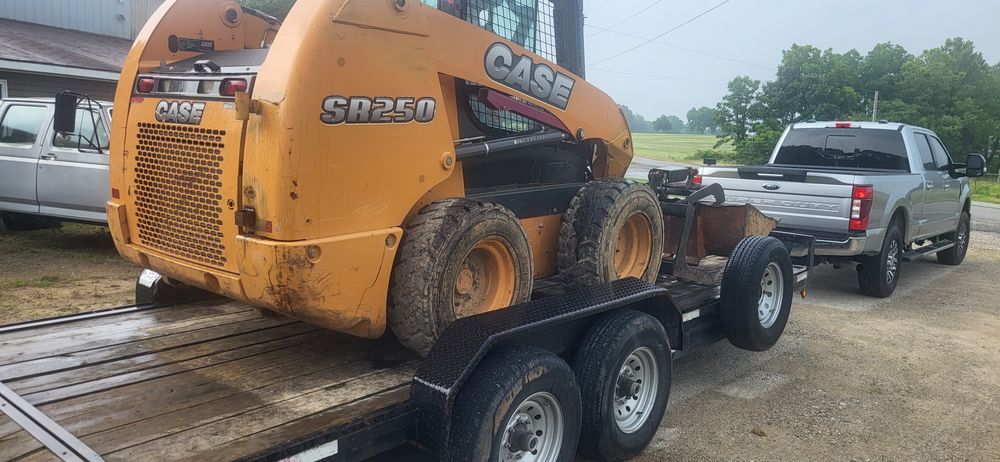 A Case skid steer loader on a trailer being towed by a gray pickup truck.