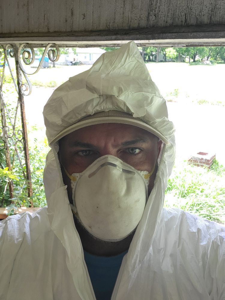 Person in white hazmat suit, respirator mask, and hood, standing outdoors.
