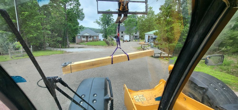 A forklift lifting a long wooden beam in a residential area. View is from inside the forklift.