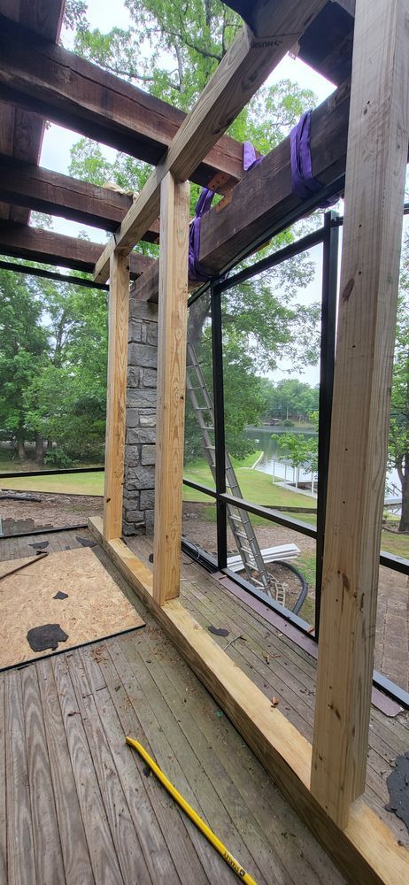 Construction of a screened porch frame, with wooden beams and a view of a lake through a window.