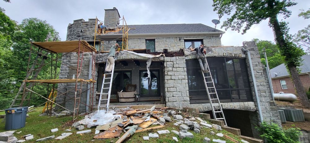 Construction on a house with stone walls. Two workers on ladders. Scaffolding is set up. Debris on the ground.