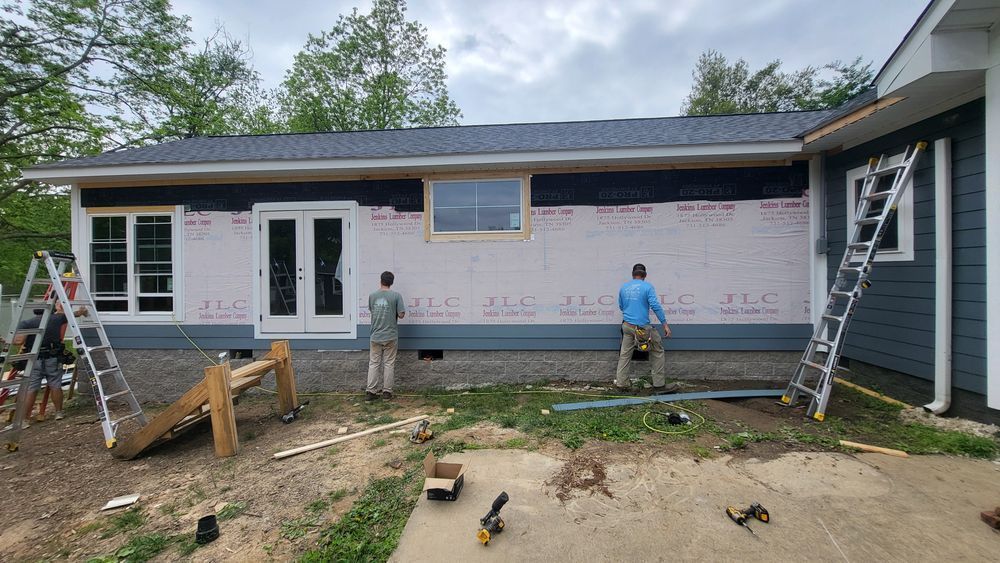 Construction workers applying siding to a house exterior. Building in progress, several ladders visible.