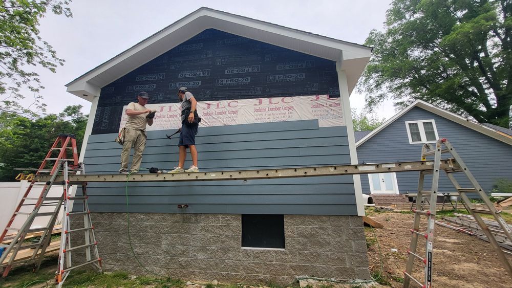 Two people installing blue siding on a house. One is on scaffolding using a tool.