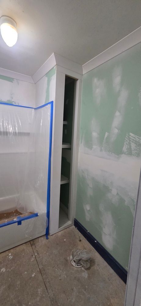 Bathroom under construction. Walls are green drywall with white trim. A built-in shelf is visible.