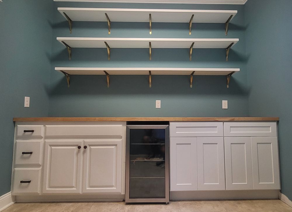 Built-in bar with white cabinets, wood countertop, wine fridge, and open shelving on a teal wall.