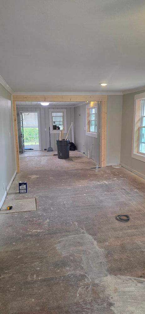 Interior of a room under renovation with exposed flooring, doorways, and windows.