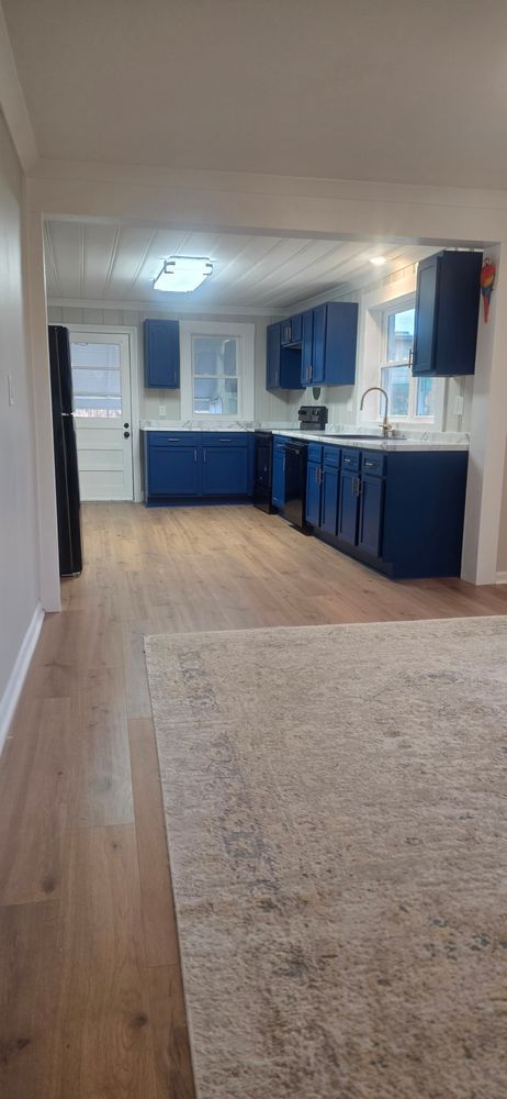 Kitchen with blue cabinets, white countertops, and wood flooring. A rug covers the foreground.