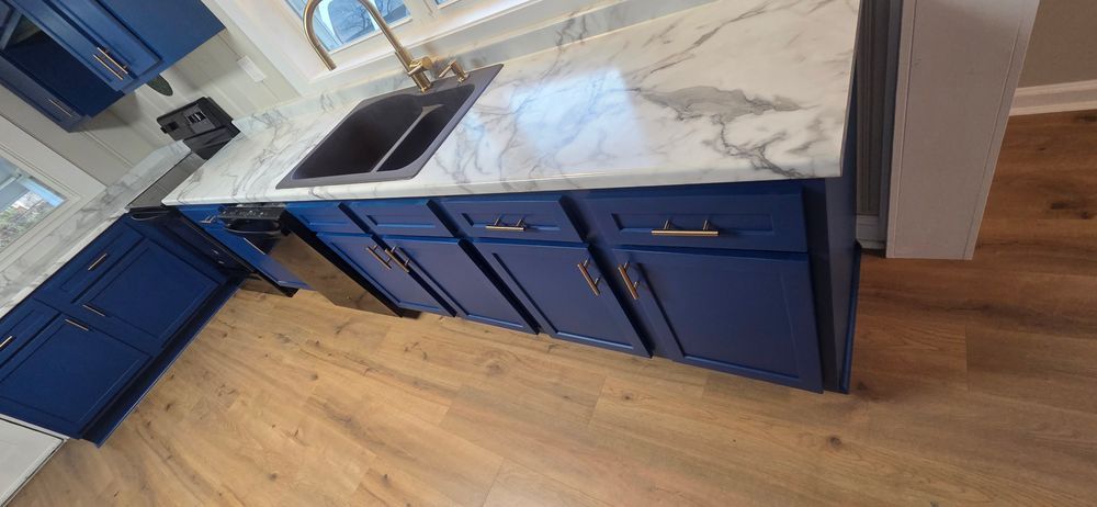Blue kitchen cabinets with white countertop and sink. Wooden floor in a kitchen.