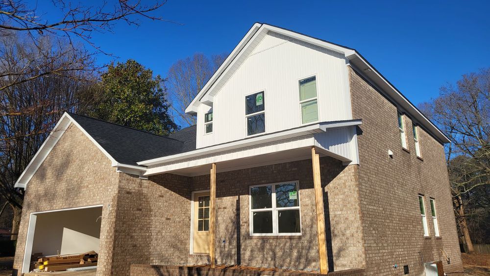 New house under construction, brick exterior, white siding, porch, and blue sky.