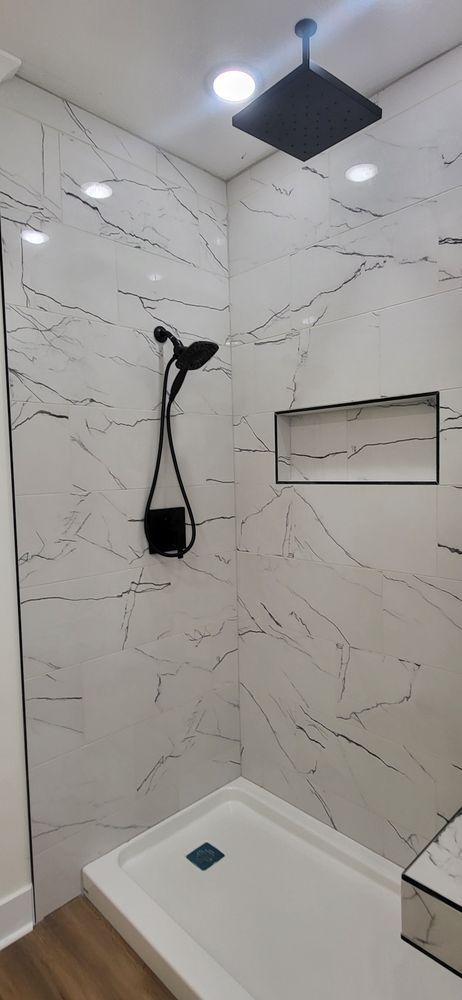Modern bathroom with white marble-like tile walls, black shower fixtures, and a recessed shelf.