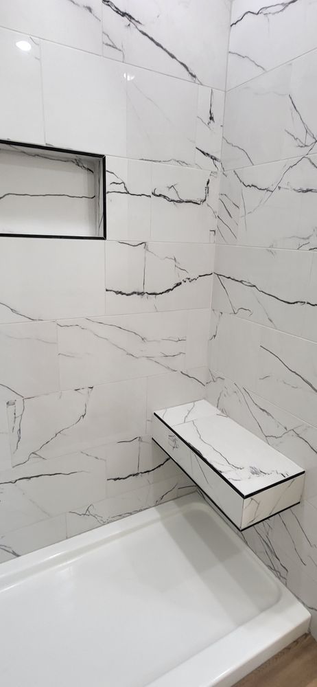 White marble-tiled shower with a built-in bench and recessed shelf; black accent trim.