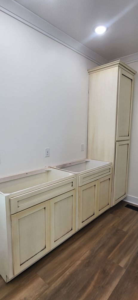 Cream-colored kitchen cabinets and tall cabinet against a white wall and dark wood-look floor.