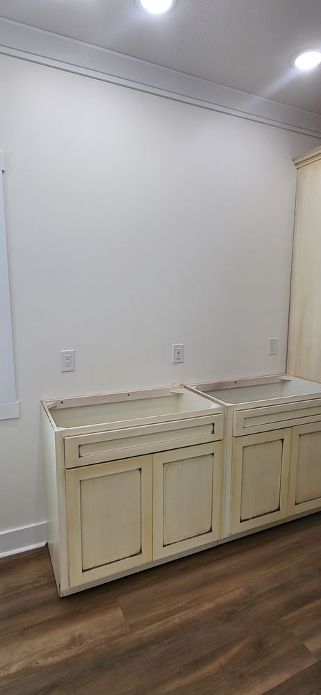 Kitchen cabinets in a room with white walls, wood floors, and overhead lighting.