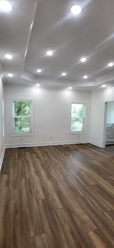 An empty room with wood floors, white walls, and a recessed ceiling with many lights. Two windows are visible.