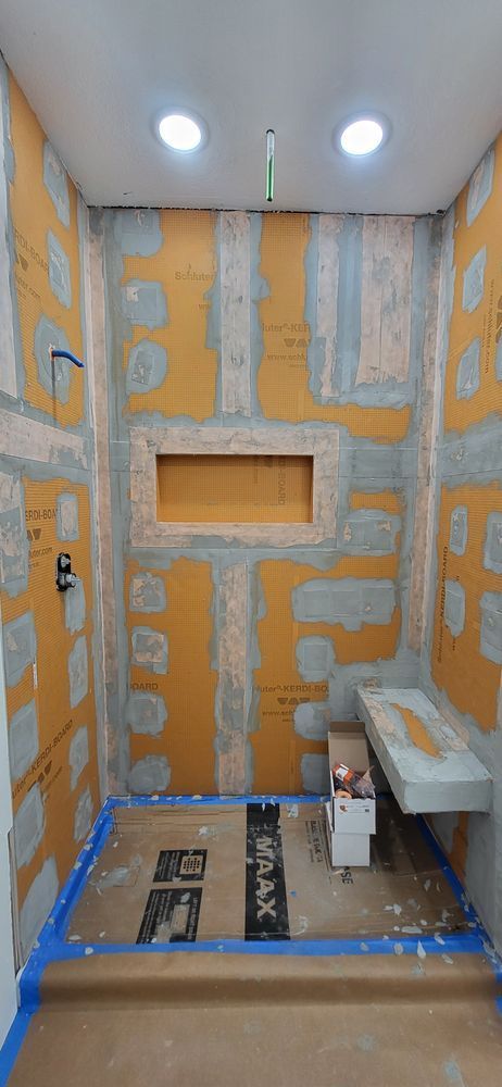 Shower in progress; orange waterproof panels installed on the walls, bench, recessed shelf, and lighting in the ceiling.