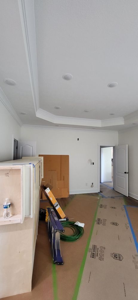 Interior room under construction with white walls, recessed lights, and exposed flooring.