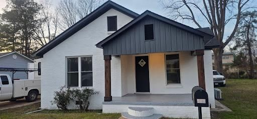 White house with a dark gray porch, black door, and brown pillars; mailbox in foreground.