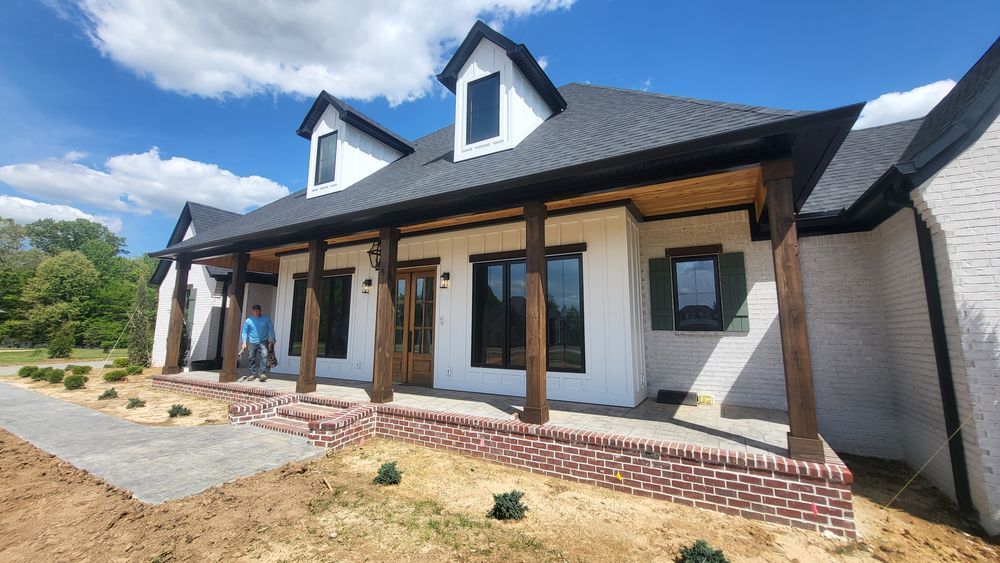 White brick house with black trim, dormers, and porch with wood columns.