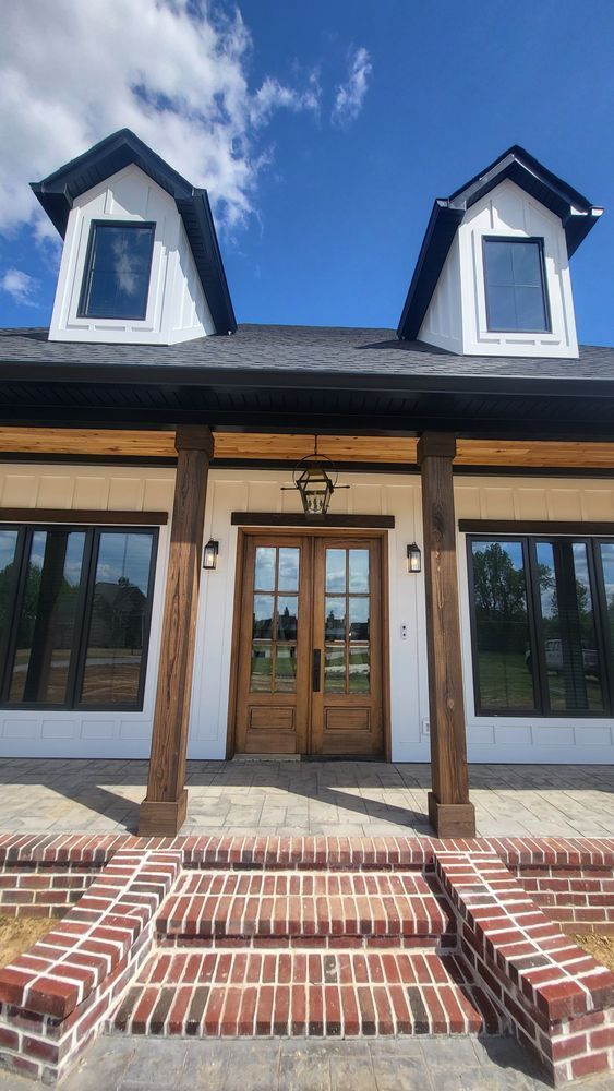 White house with brick steps, brown wooden columns, and two dormers under a blue sky.