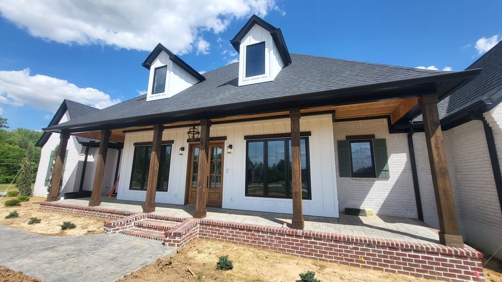 White brick house with black trim, dormers, and a wooden porch. Blue sky in the background.